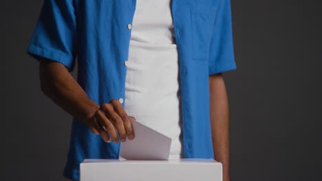Close-Up-Of-Man-Casting-Vote-Into-Election-Ballot-Box-Against-Black-Background-In-Slow-Motion